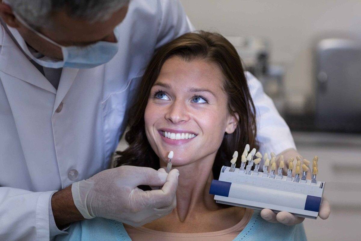 Dentist comparing veneer shades with a smiling patient during a cosmetic dental consultation